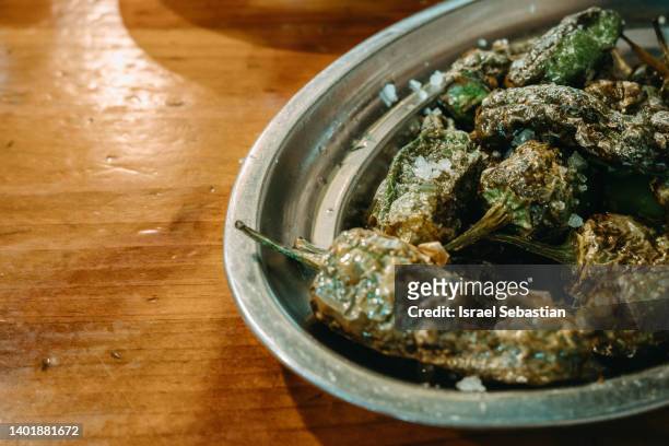 close-up view of a tray of fried padron peppers on a wooden table. - olive pimento stock pictures, royalty-free photos & images