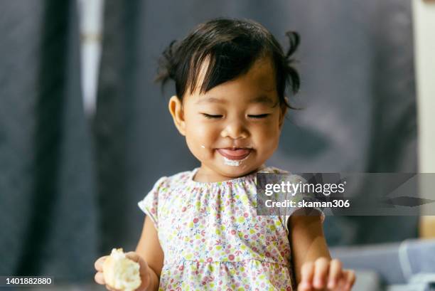 close-up candid shot asian baby girl enjoys eating sweet dessert at home. domestic life copyspace concept - asian baby - fotografias e filmes do acervo
