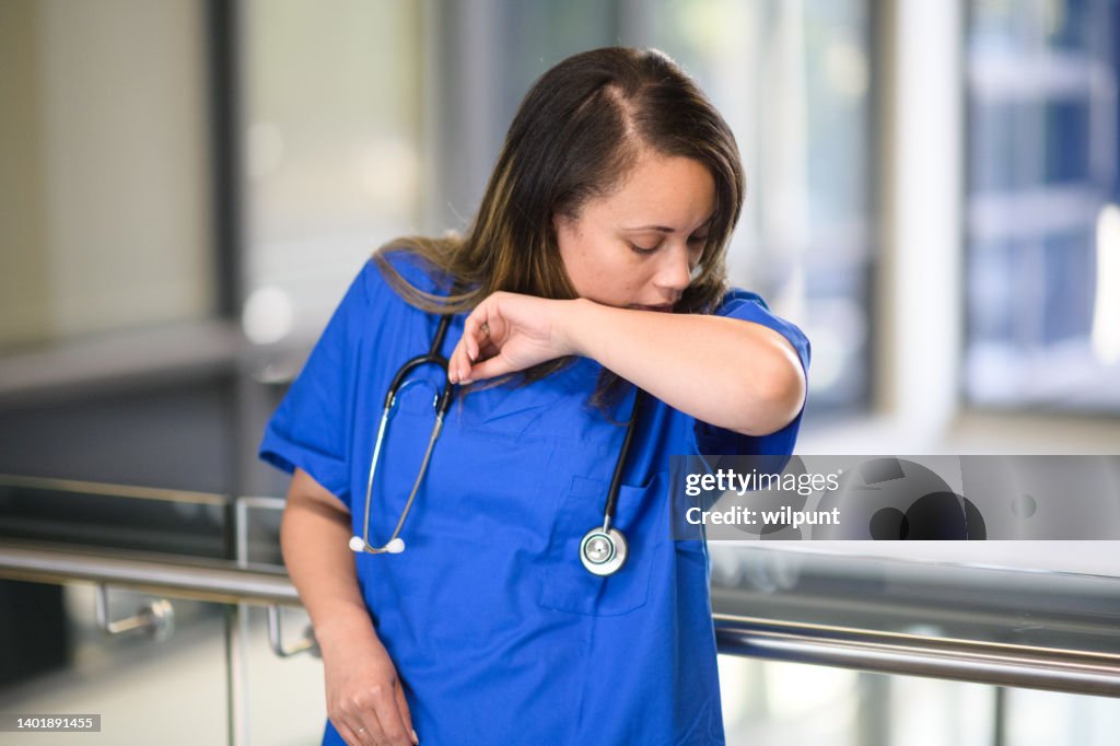 Side view Female Nurse Doctor in scrubs Portrait in hospital coughing sneezing in elbow