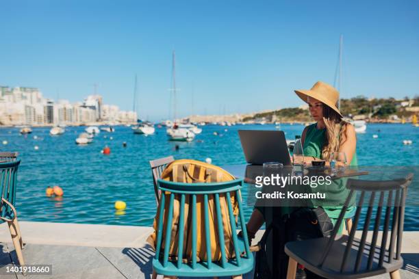 a business woman sitting in a coffee shop on the dock, not far from the sea and working on a laptop - malta business stock pictures, royalty-free photos & images