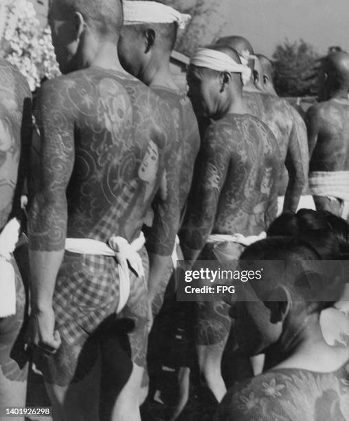 Men, standing in line, showcase their bodysuit tattoo designs at a tattoo convention in Japan, May 1950.