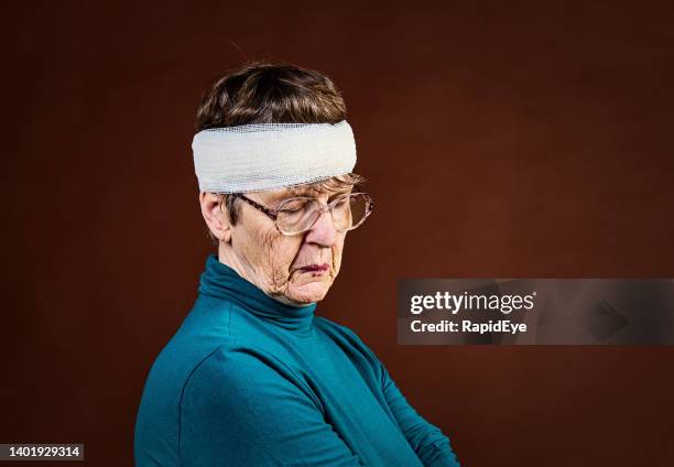 bandage wrapped around her head, an injured, depressed senior woman looks downcast - senior women wine stock pictures, royalty-free photos & images