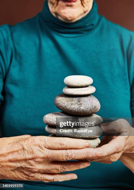 balance im alter finden: die hände älterer frauen stützen einen stapel flacher steine im zen-stil - stone hand stock-fotos und bilder
