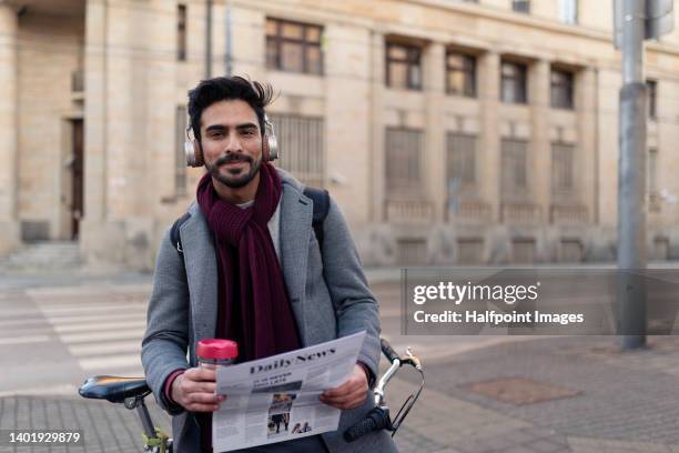 young handsome middle eastern man in business clothes sitting in his bicycle, reading newspaper and drinking coffee. - handsome middle eastern men stock-fotos und bilder