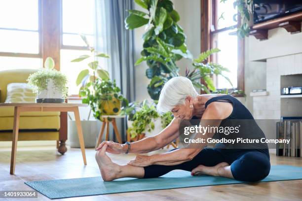 ältere frau, die während einer yoga-sitzung dehnübungen in ihrem wohnzimmer macht - zehenspitzen berühren stock-fotos und bilder