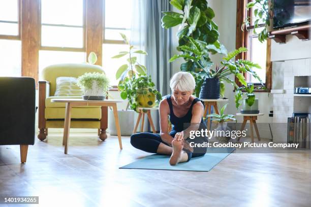 ältere frau, die sich während einer yoga-sitzung in ihrem wohnzimmer dehnt - zehenspitzen berühren stock-fotos und bilder