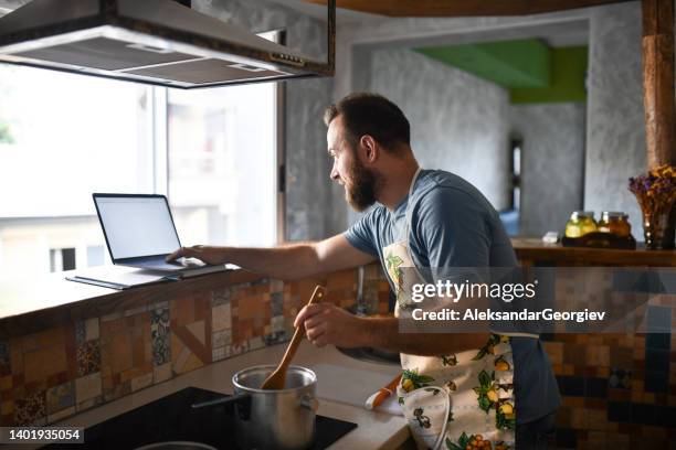 bearded male stirring stew while working on laptop from home - fast typing stock pictures, royalty-free photos & images