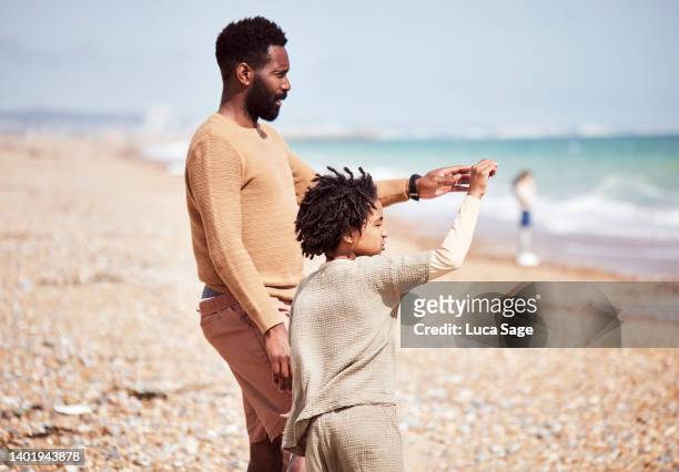 father and son looking out to sea, on the beach, on a family day out - seven point stock pictures, royalty-free photos & images