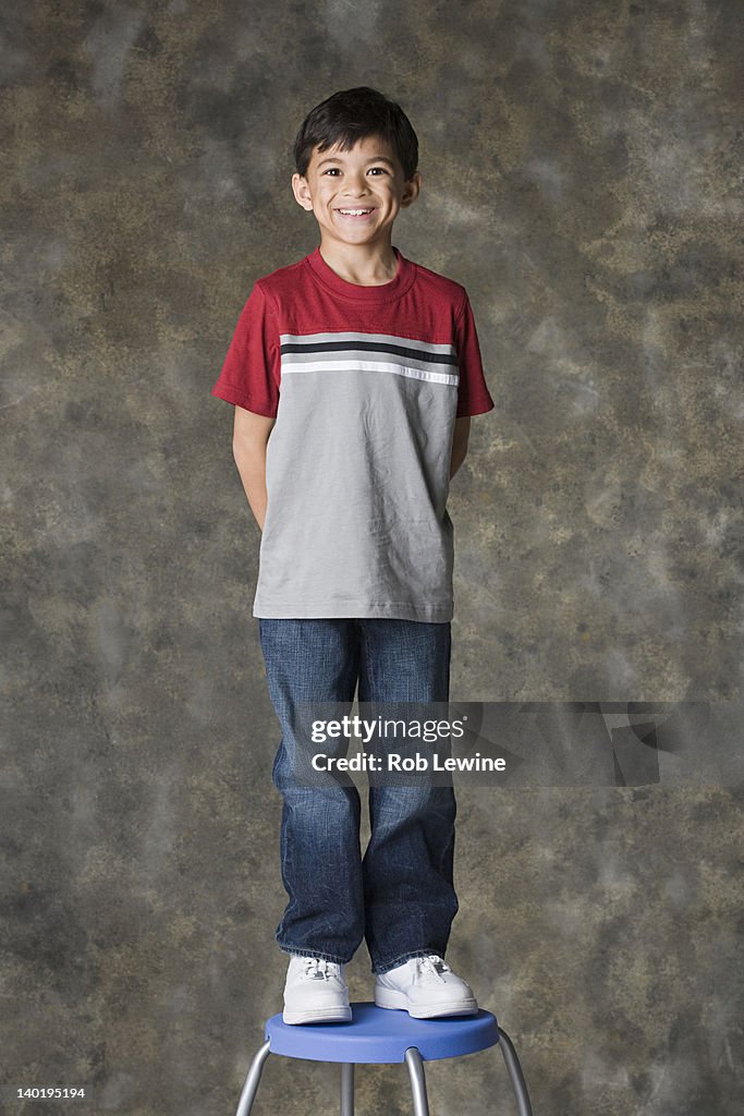 Portrait of smiling boy (8-9) standing on stool, studio shot