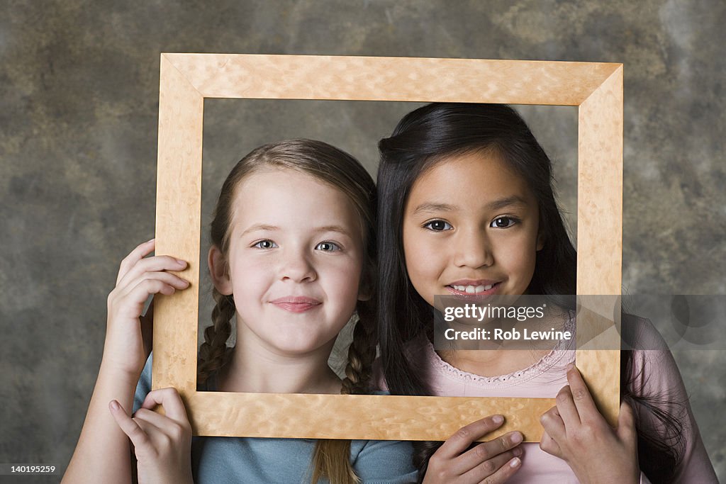 Portrait of girls (8-9) looking through picture frame, studio shot