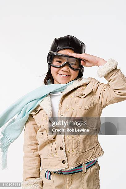 studio portrait of saluting girl (8-9) wearing aviator's cap and flying goggles - aviation hat stock pictures, royalty-free photos & images