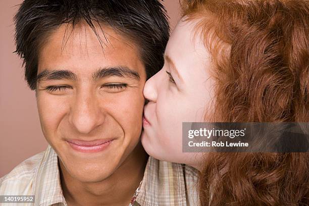 portrait of teenage (16-17) girl kissing teenage boy (16-17) - sfondo beige foto e immagini stock