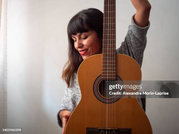 brown woman with red lips holds acoustic guitar in a white room - guitarra acústica fotografías e imágenes de stock