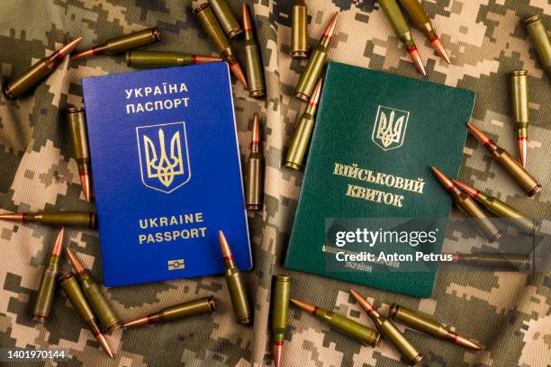 ukrainian passport and a military certificate on the background of the camouflage of the ukrainian army. war in ukraine - visa card stock-fotos und bilder