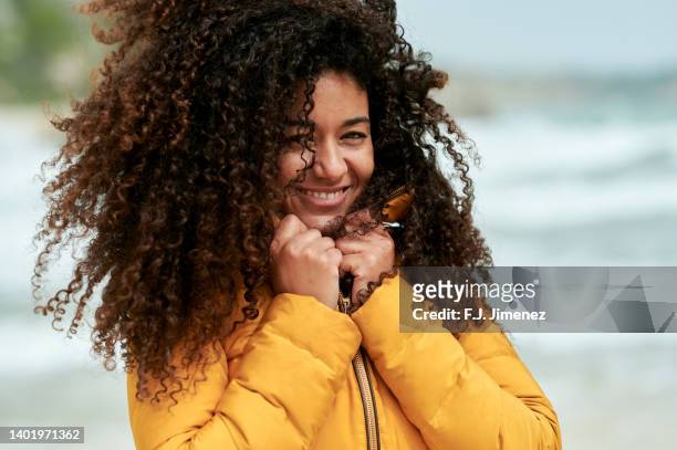 portrait of woman with afro hair on the beach in winter - natural hair stock-fotos und bilder