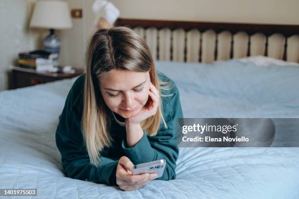 blond woman looks at her smartphone screen, writes a message and makes a video call - online dating 個照片及圖片檔