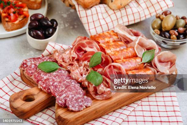 food antipasto prosciutto ham, salami, olives and bread and tomato and basil bruschetta charcuterie board. two glasses of white wine or prosecco - plateau photos et images de collection