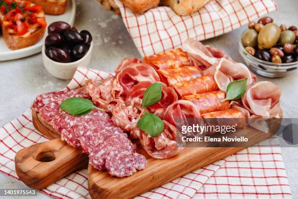 food antipasto prosciutto ham, salami, olives and bread and tomato and basil bruschetta charcuterie board. two glasses of white wine or prosecco - cutting board stock pictures, royalty-free photos & images
