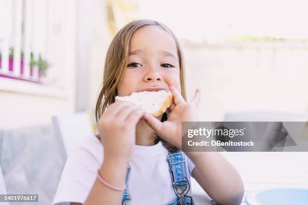 little blonde-haired girl eating a piece of toast with cocoa cream spread, her face smeared with chocolate. - girls laughing eating sandwich stock-fotos und bilder