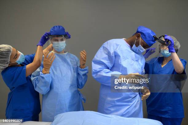 medical teamwork surgeons getting face shield fitted by surgical assistants before operating - operating gown stock pictures, royalty-free photos & images