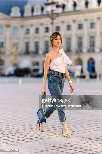 Heart Evangelista wears a one/off-shoulder rib ruffled / pleated white top, blue denim high-waist cropped jeans / pants with hems, a blue Chanel bag,...