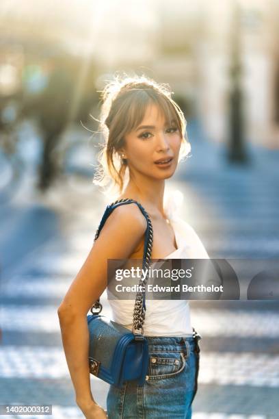 Heart Evangelista wears a one/off-shoulder rib ruffled / pleated white top, blue denim high-waist jeans / pants, a blue Chanel bag, during a street...