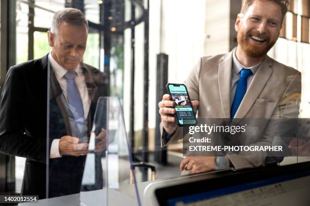 two business colleagues with a booking app on the phone screen seen during hotel check in - making a reservation stock pictures, royalty-free photos & images