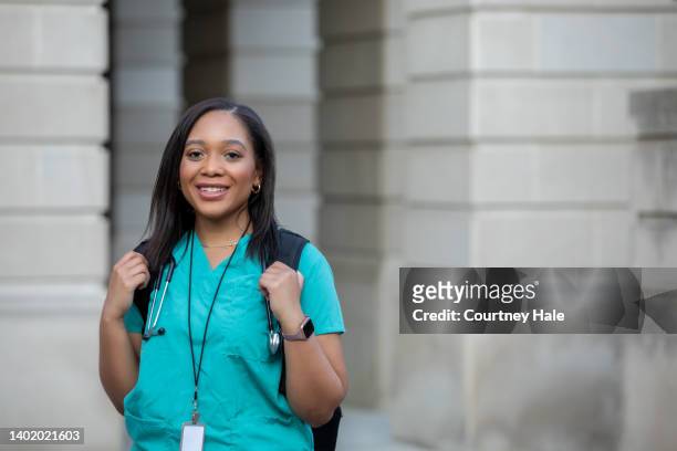 young african american woman smiles while walking on campus of medical school or nursing college - lovely professional university stock pictures, royalty-free photos & images