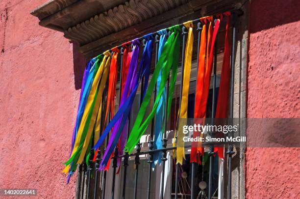 satin ribbons in rainbow colors hanging from the metal security bars over a window on a spanish colonial house - rainbow ribbon stock pictures, royalty-free photos & images