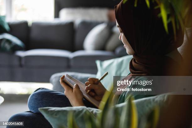 side view of young woman writing in a diary about her day - burka stock pictures, royalty-free photos & images