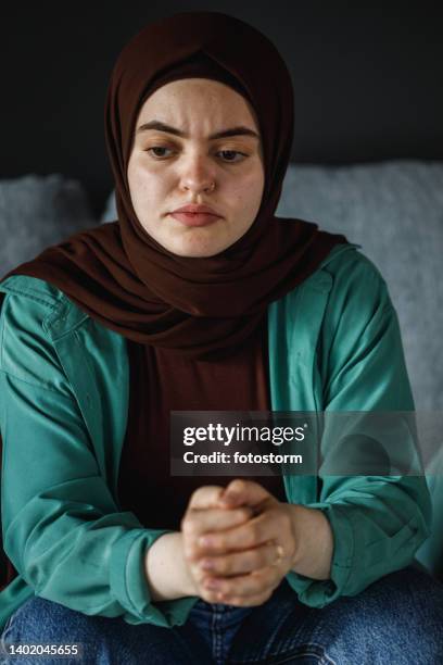 distraught young woman sitting with hands clasped, worrying - burka stock pictures, royalty-free photos & images
