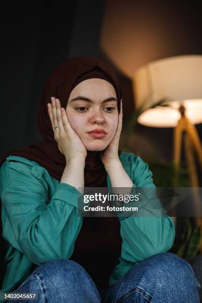 distraught young woman sitting with head in hands, contemplating - burka stock pictures, royalty-free photos & images