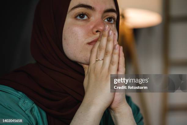 worried young woman in hijab sitting with praying hands, contemplating - burka stock pictures, royalty-free photos & images