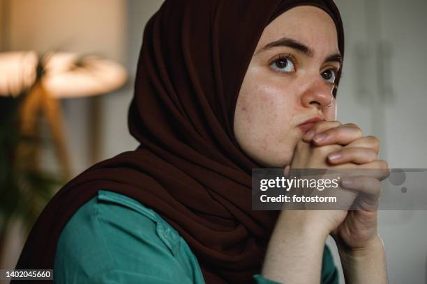 worried young woman sitting with hands clasped in front of face, contemplating - burka stock pictures, royalty-free photos & images