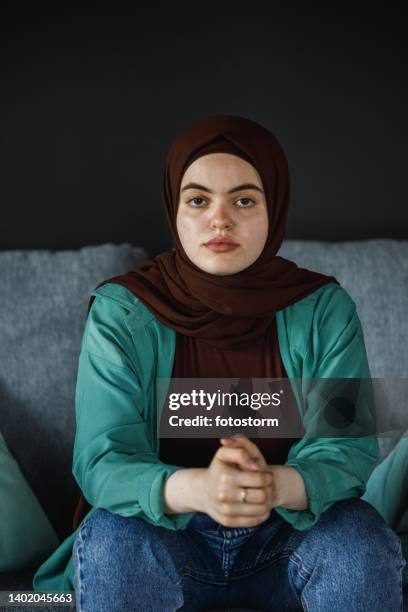 young woman sitting on the sofa, cracking her knuckles, looking at camera - burka stock pictures, royalty-free photos & images