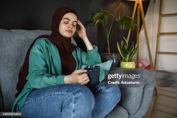 young woman trying to calm down while relaxing on the sofa and having morning coffee - burka stock pictures, royalty-free photos & images