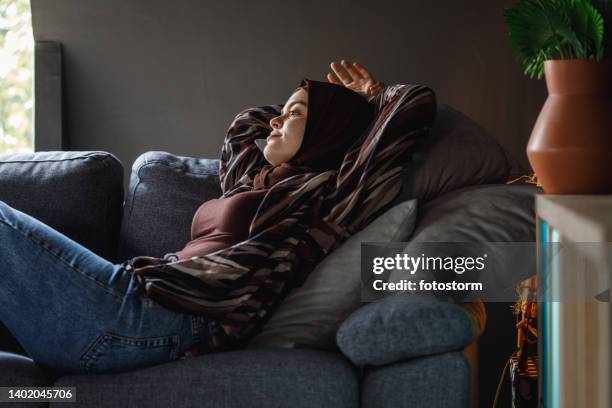 young woman lounging on the sofa with hands behind head, pondering - burka stock pictures, royalty-free photos & images