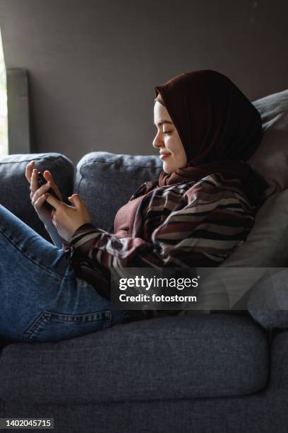 side view of young woman relaxing on the sofa and using smart phone - burka stock pictures, royalty-free photos & images