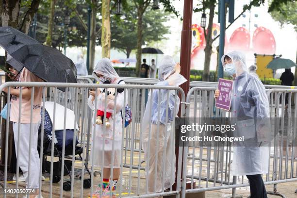 Resort staff holds a safe distancing sign as visitors wait in line to enter a store at Shanghai Disney Resort on June 10, 2022 in Shanghai, China....