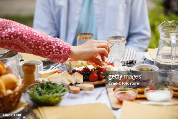 mujer buscando un trozo de queso servido en una tabla de charcutería - charcutería fotografías e imágenes de stock