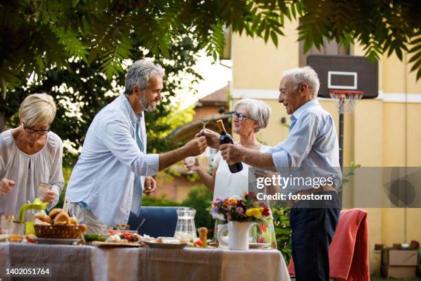 man giving his friend bottle opener and a bottle or red wine to open during a dinner party - vinger bildbanksfoton och bilder