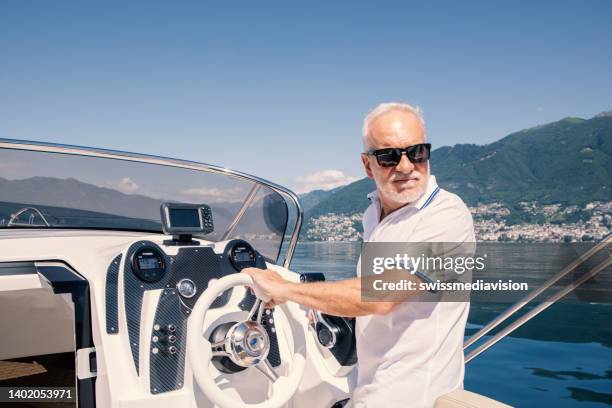 senior man driving a speed boat on a lake in summer - motorboot varen stockfoto's en -beelden