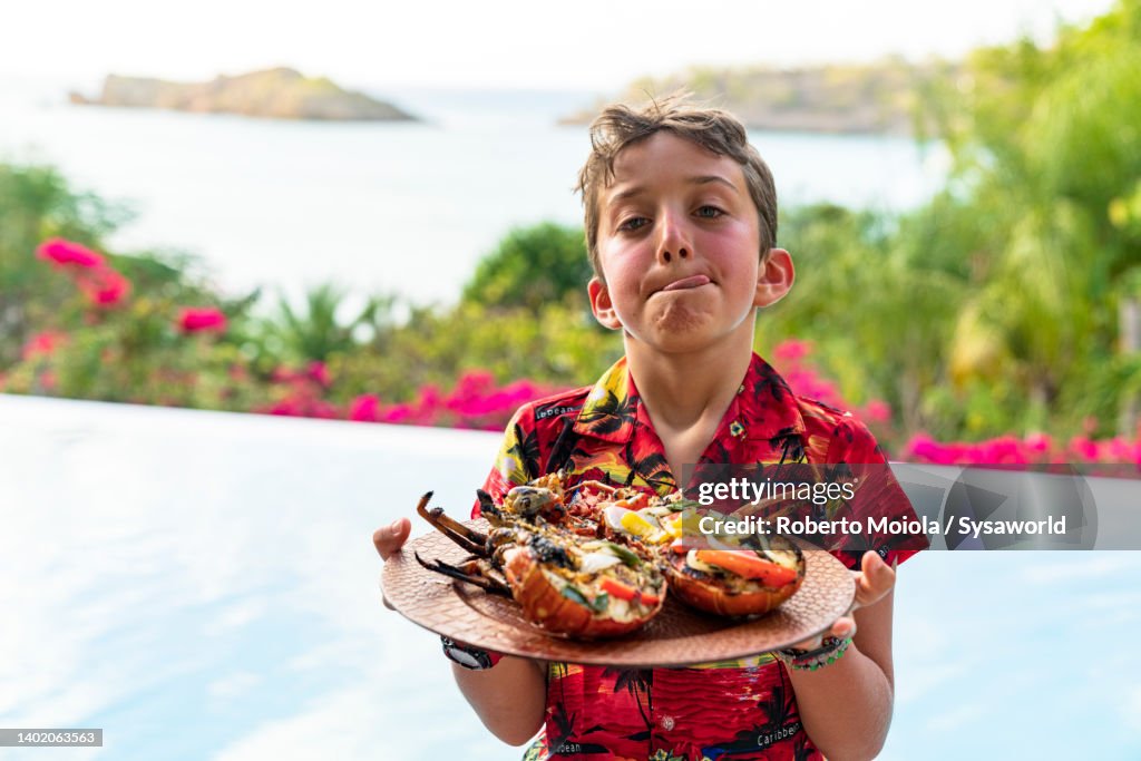 Happy boy making funny face holding a plate with lobsters