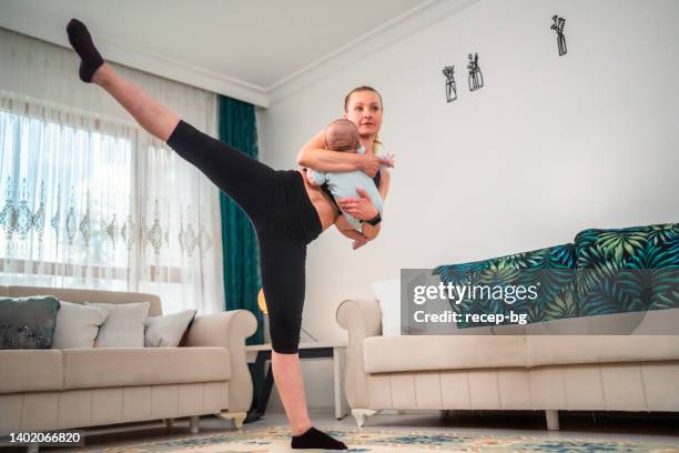 madre entrenando en casa mientras cuida a su bebé recién nacido en la sala de estar - new sport content fotografías e imágenes de stock