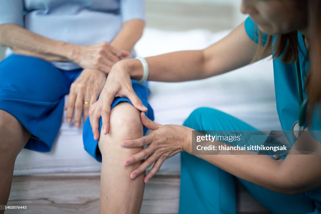Female nurse home caregiver checking a knee to senior woman