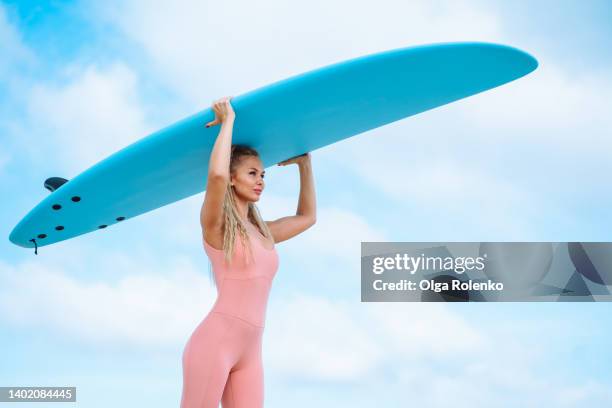 female surfer with surfboard above the head, trying to catch waves on the beach - surf board foto e immagini stock