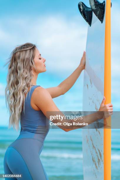 female surfer standing on the beach near sea looking at her surfboard - curly waves stock pictures, royalty-free photos & images