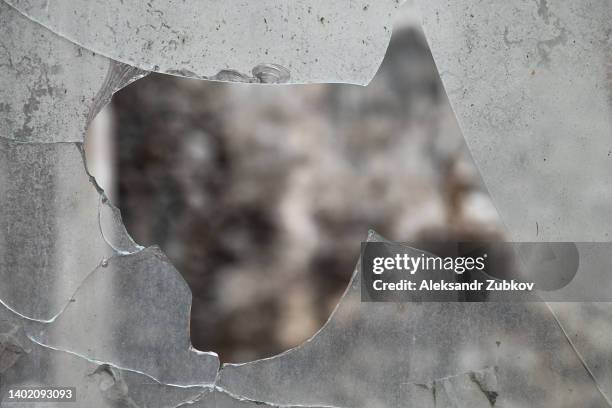 dirty broken glass in the window frame. a ruined abandoned dilapidated building or house. damage to a bombed building, the consequences of vandalism. - shattered glass fotografías e imágenes de stock