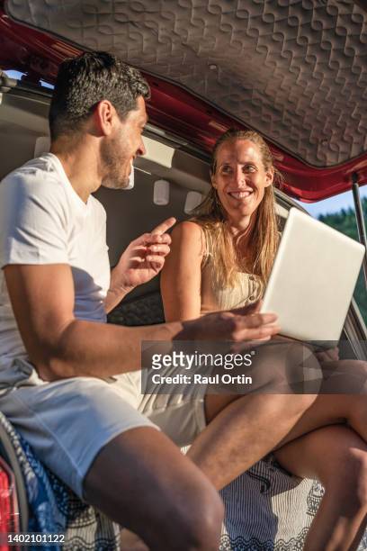 couple talking while using laptop sitting in camper van - labor camp fotografías e imágenes de stock