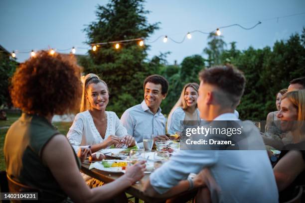 friends and family eating dinner outdoors on warm summer night - outdoor dinner party stock pictures, royalty-free photos & images